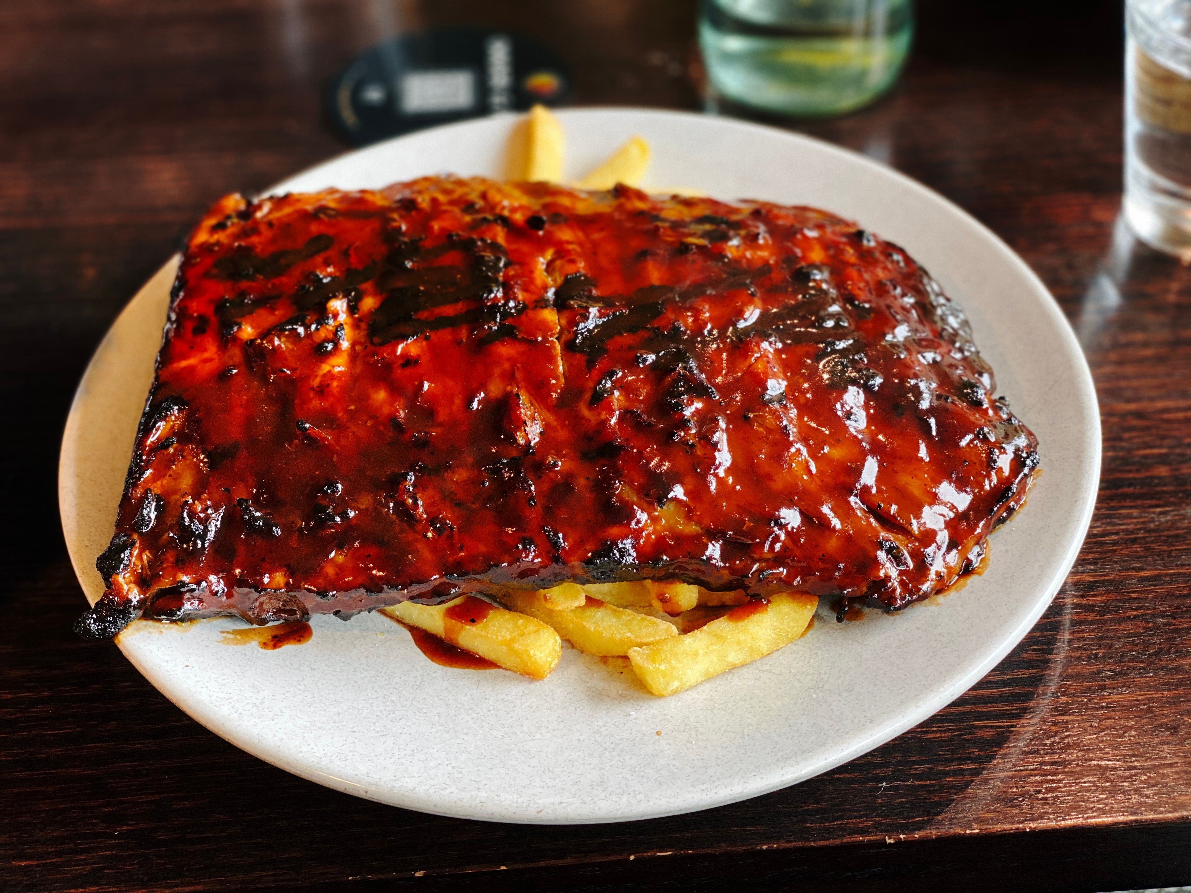 A photo of a half rack of ribs slathered in sauce sitting on top of hot chips.