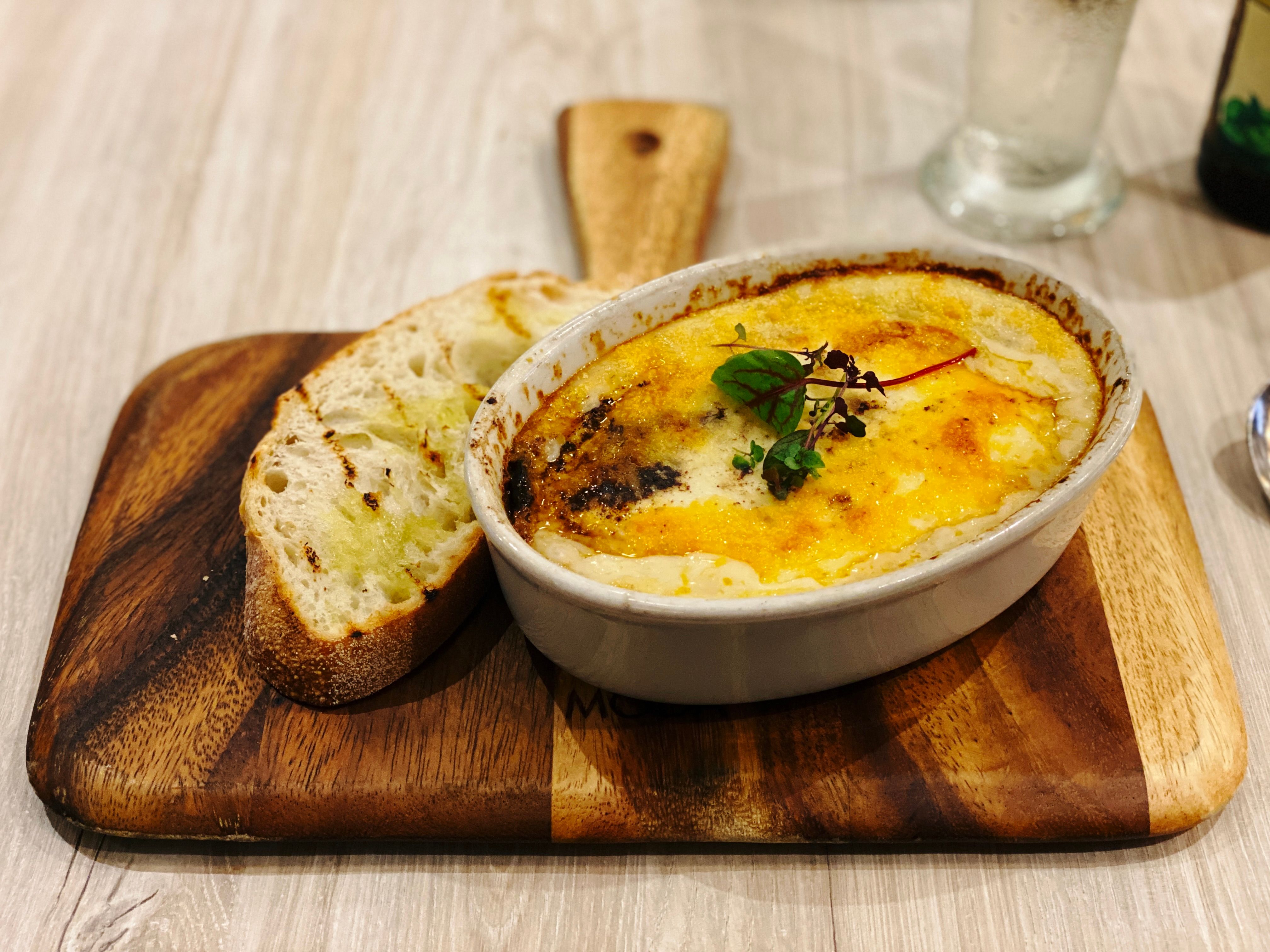 A photo of an oval-shaped ceramic dish with moussaka in it, alongside a slice of bread.