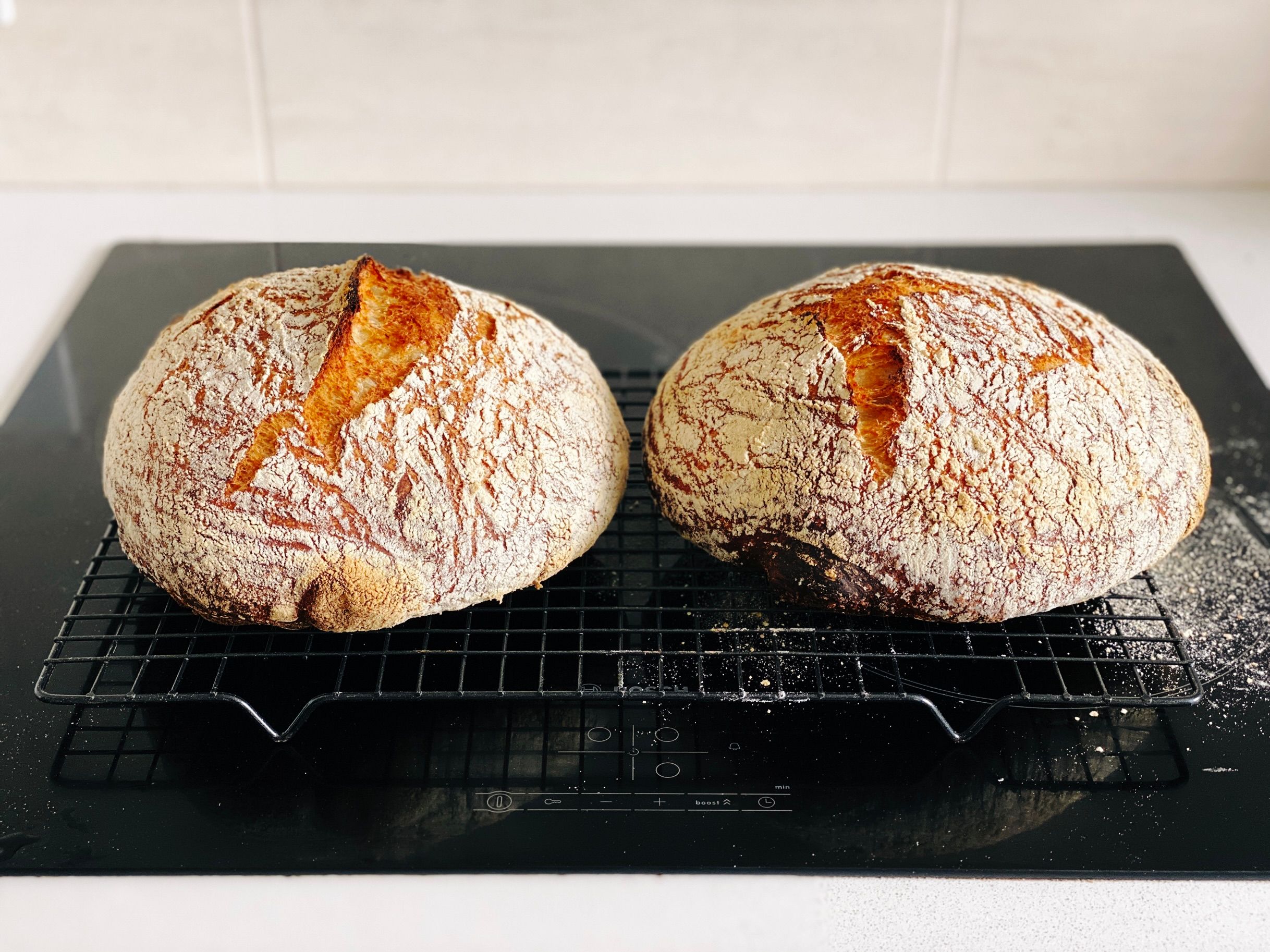 A photo of two round golden-brown loaves of bread sitting on a cooling rack.