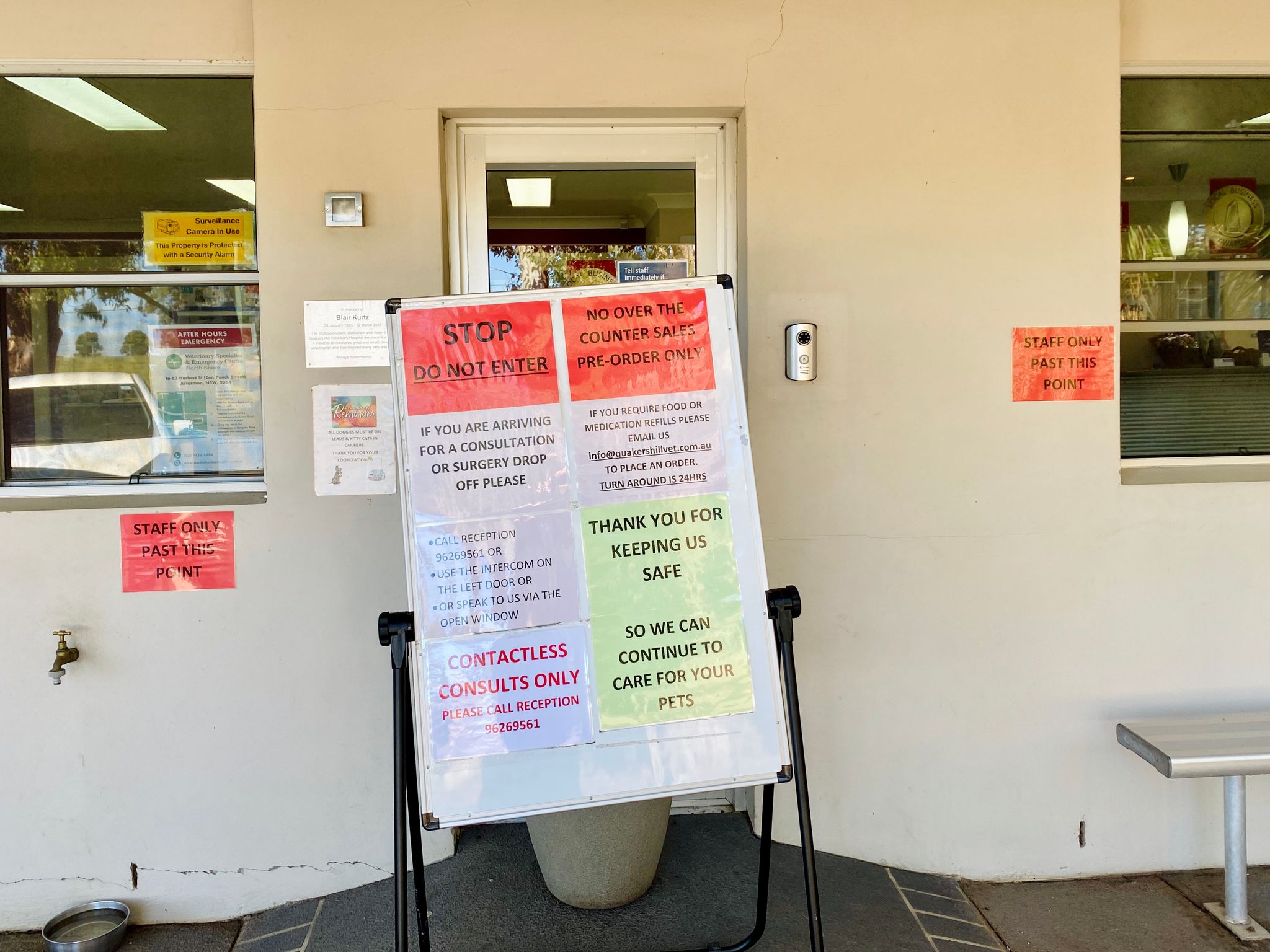 A photo of the outside of a building with a bunch of signs on it about social distancing and a board sitting directly in front of the doorway with more signs on it.