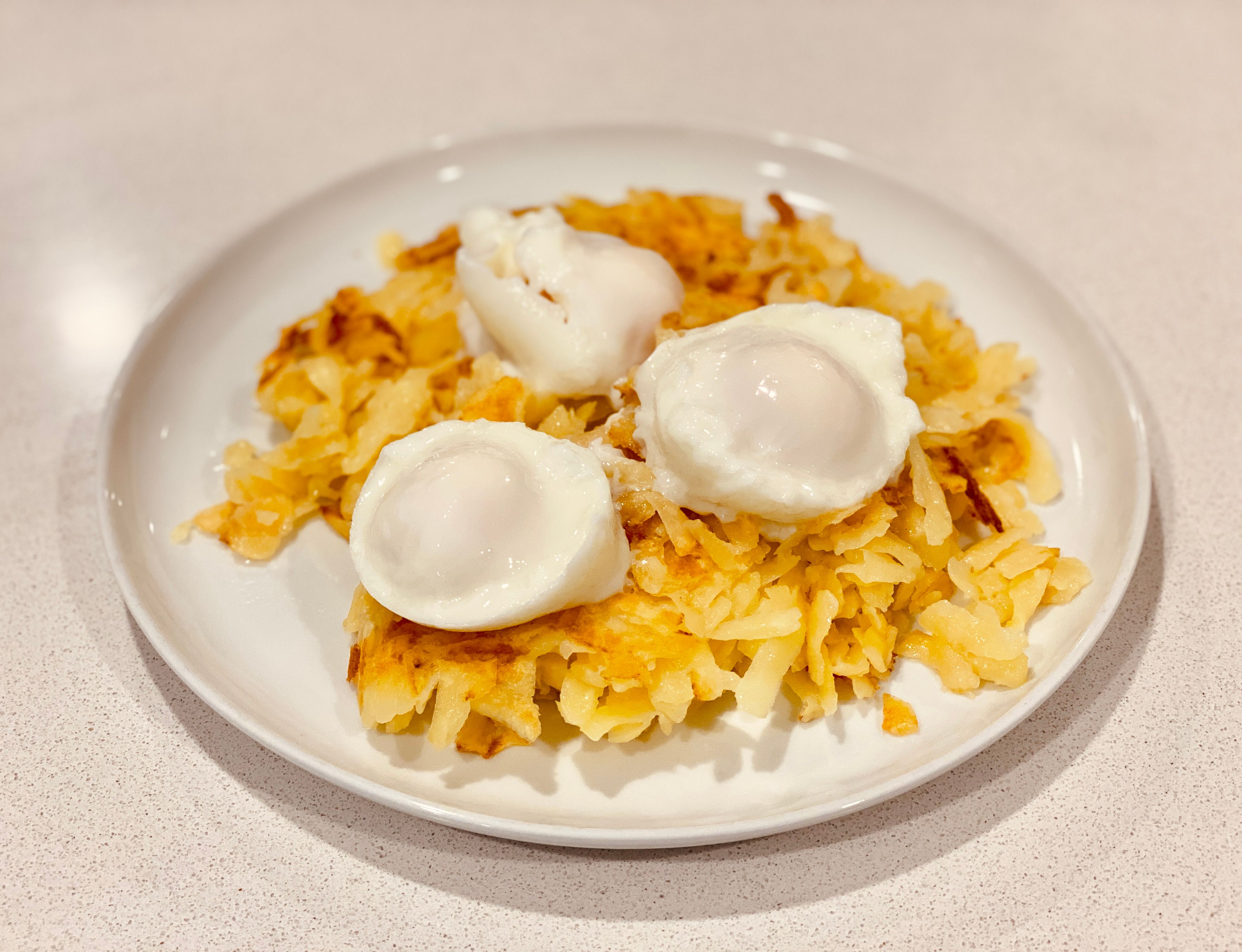 A photo of a plate with a fallen-apart rösti on it, with three poached eggs sitting on top.