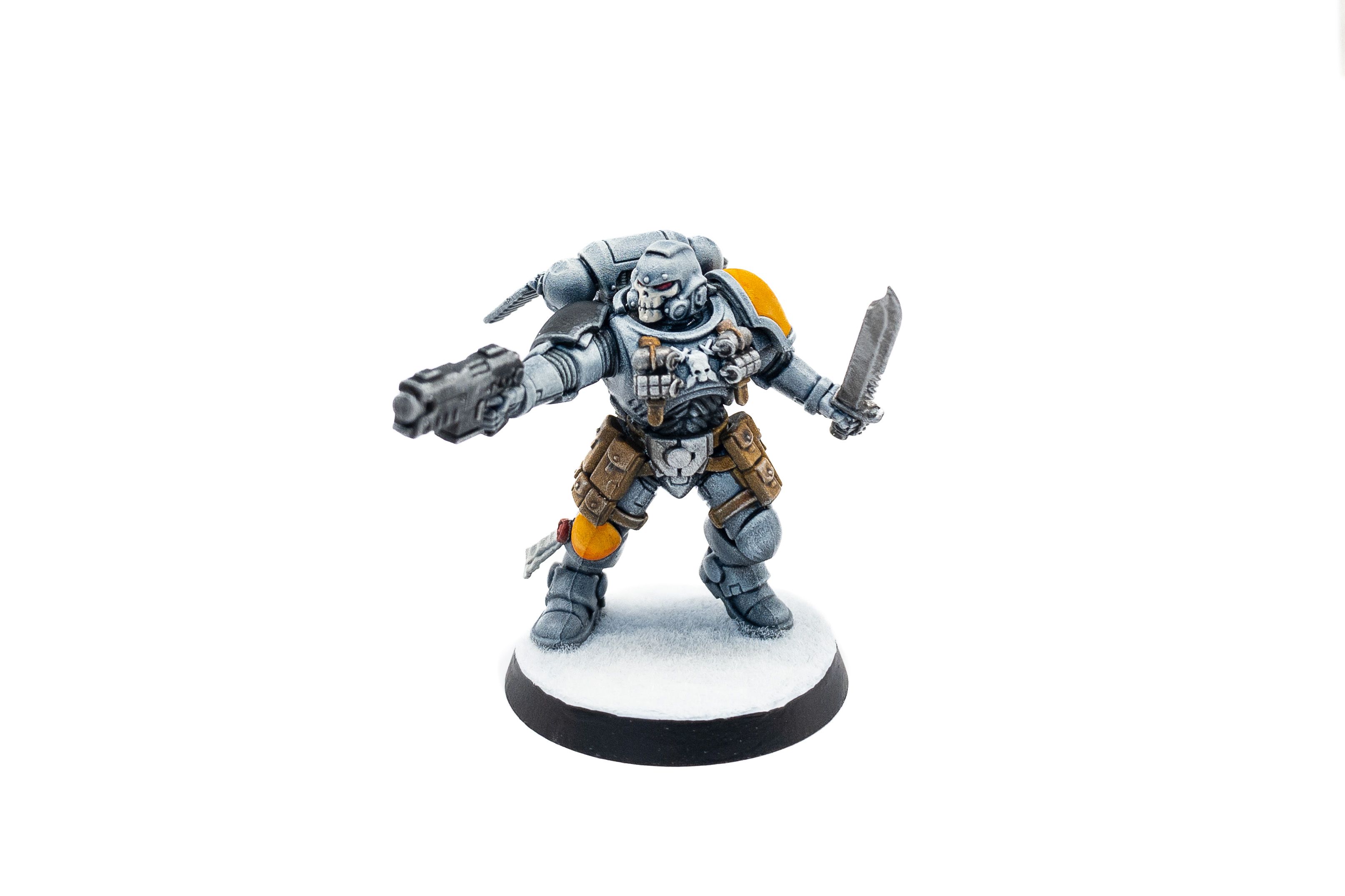 A photo of a Space Marine Reiver painted in Space Wolves colours (primarily blue-grey with a yellow shoulder pad). He's heavily-armoured with a helmet that has a skull design on the front, and is aiming a pistol and wielding a huge combat knife in the other hand.