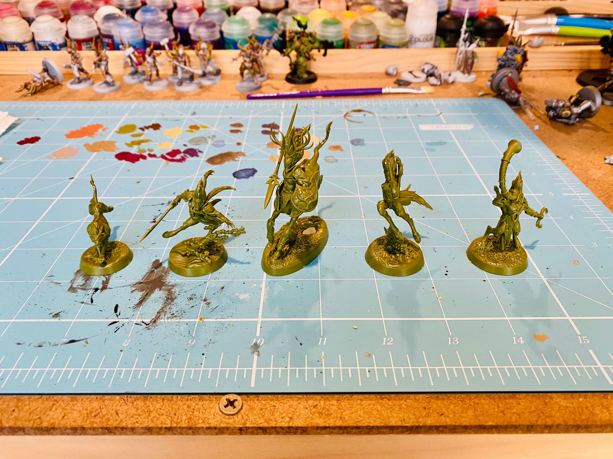 A photo of five miniatures in dark green plastic, four look like elves but with centaur legs and cloven feet, and they're all in very dynamic fluid poses. The fifth is a chimera-looking animal that's mid-run.