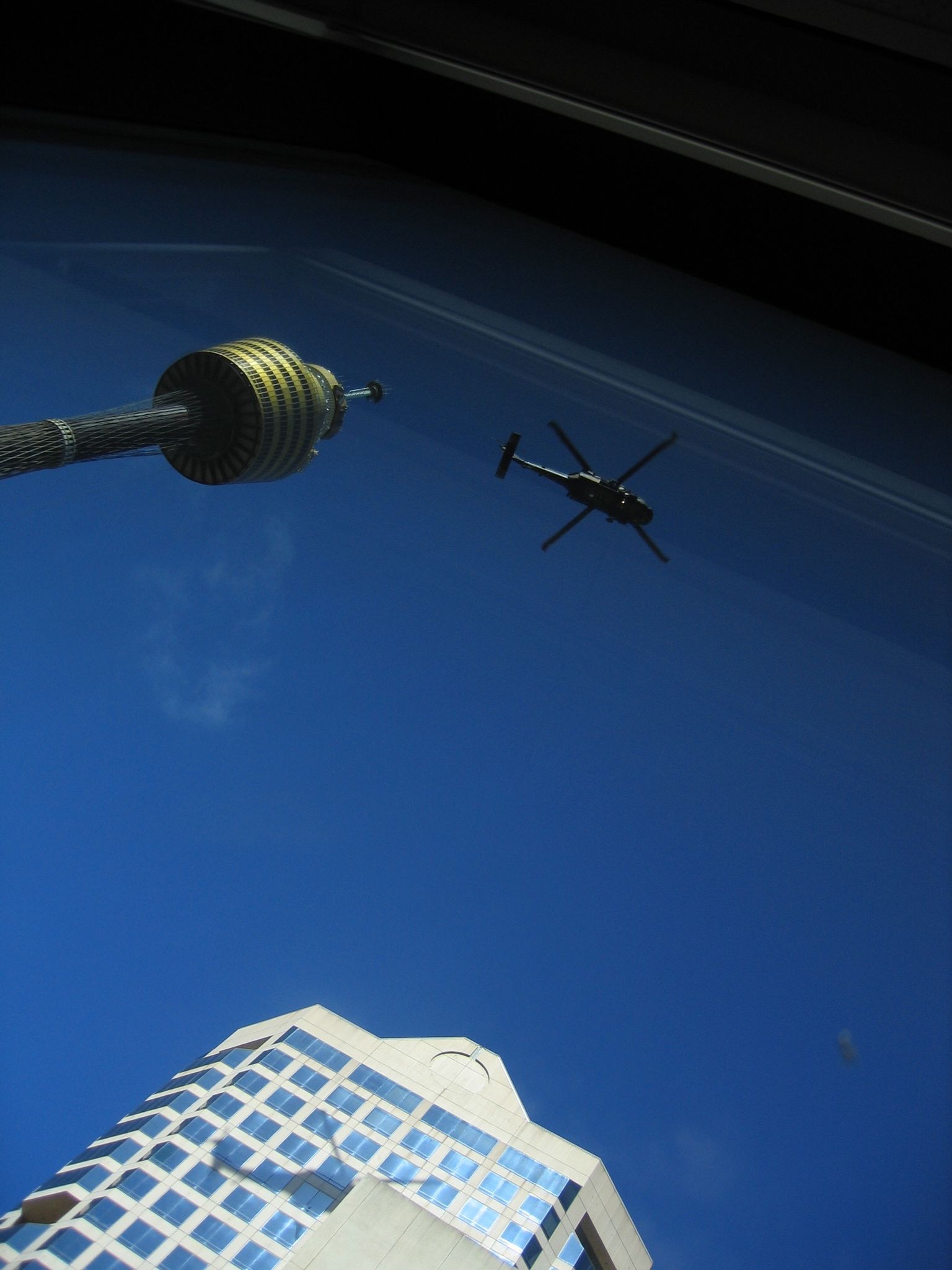A photo taking from as close to the window as possible looking directly upwards, with a Blackhawk helicopter almost directly above, and Centrepoint Tower visible at the left.
