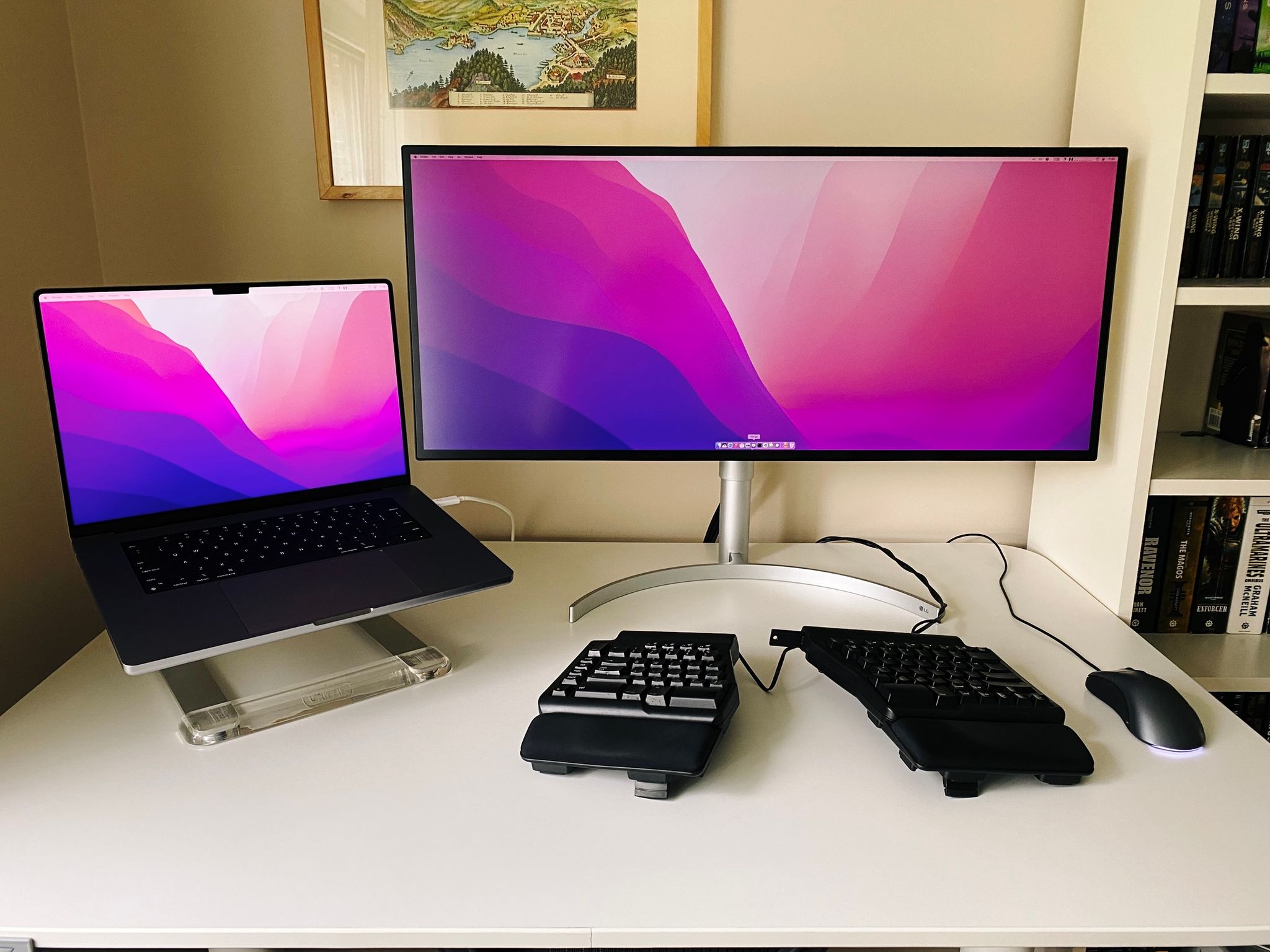 A photo of my new desk setup: a 34K LG Ultrawide monitor with a Space Grey M1 Max MacBook Pro off to the left sitting on a laptop stand, with one single cable coming out of the laptop that provides power, USB, and video.