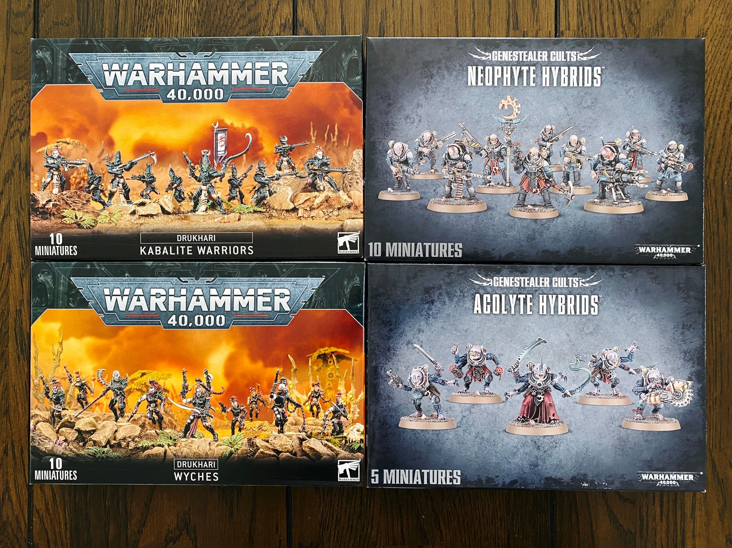 A photo of four boxes of Warhammer 40,000 miniatures. Kabalite Warriors and Wyches for the Drukhari (think sadistic space elves), and Neophyte Hybrids and Acolyte Hybrids for the Genestealer Cults (the Neophytes are broadly human but with heads that are slightly too bulbous and alien-looking, the Acolytes are humanoid but with 3 arms and heads more like the alien from the movie Alien).