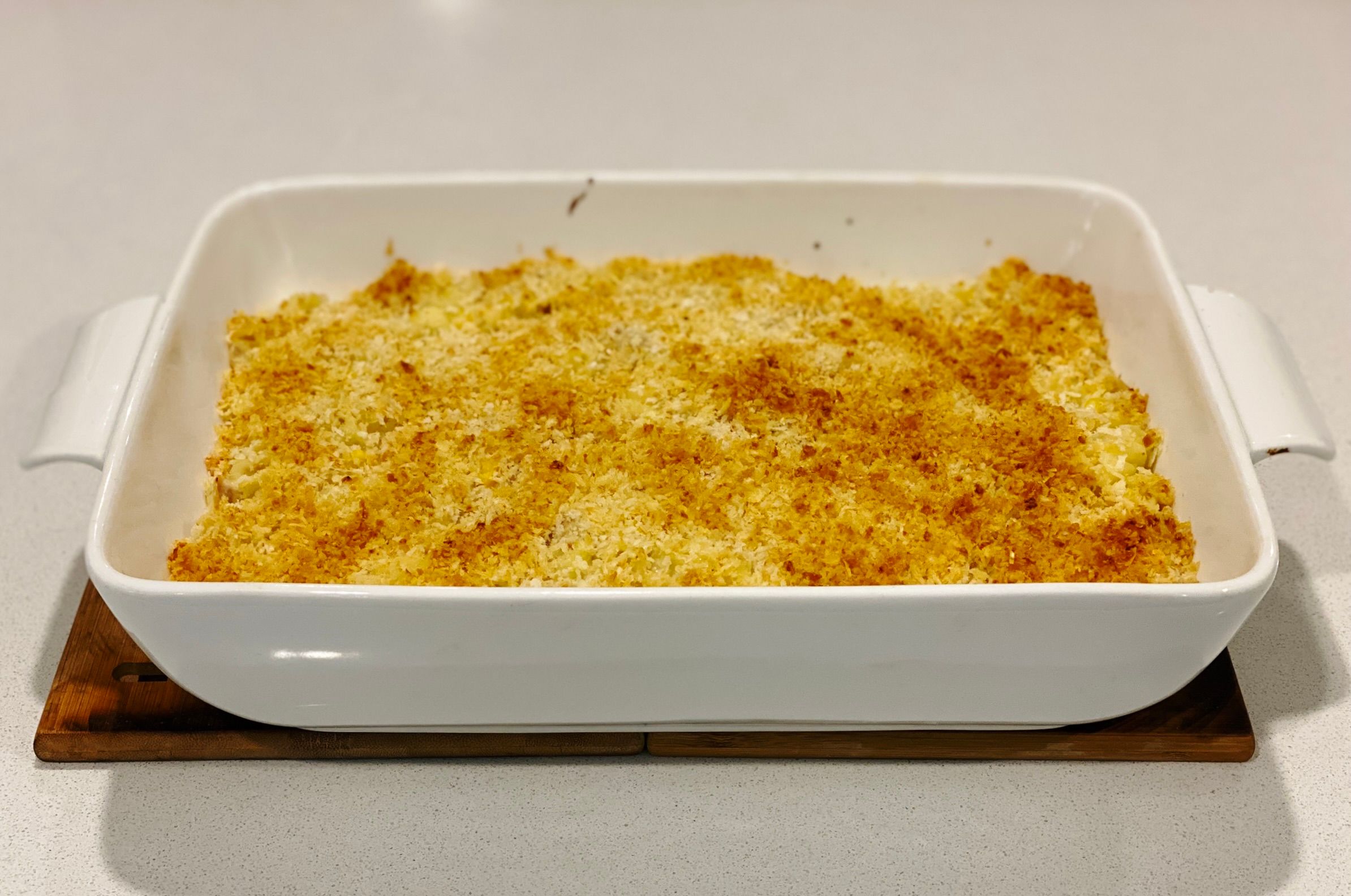 A photo of a big white rectangular casserole dish with food in it, but you can't make out what's underneath the crunchy golden brown panko breadcrumb topping. It looks amazing though.