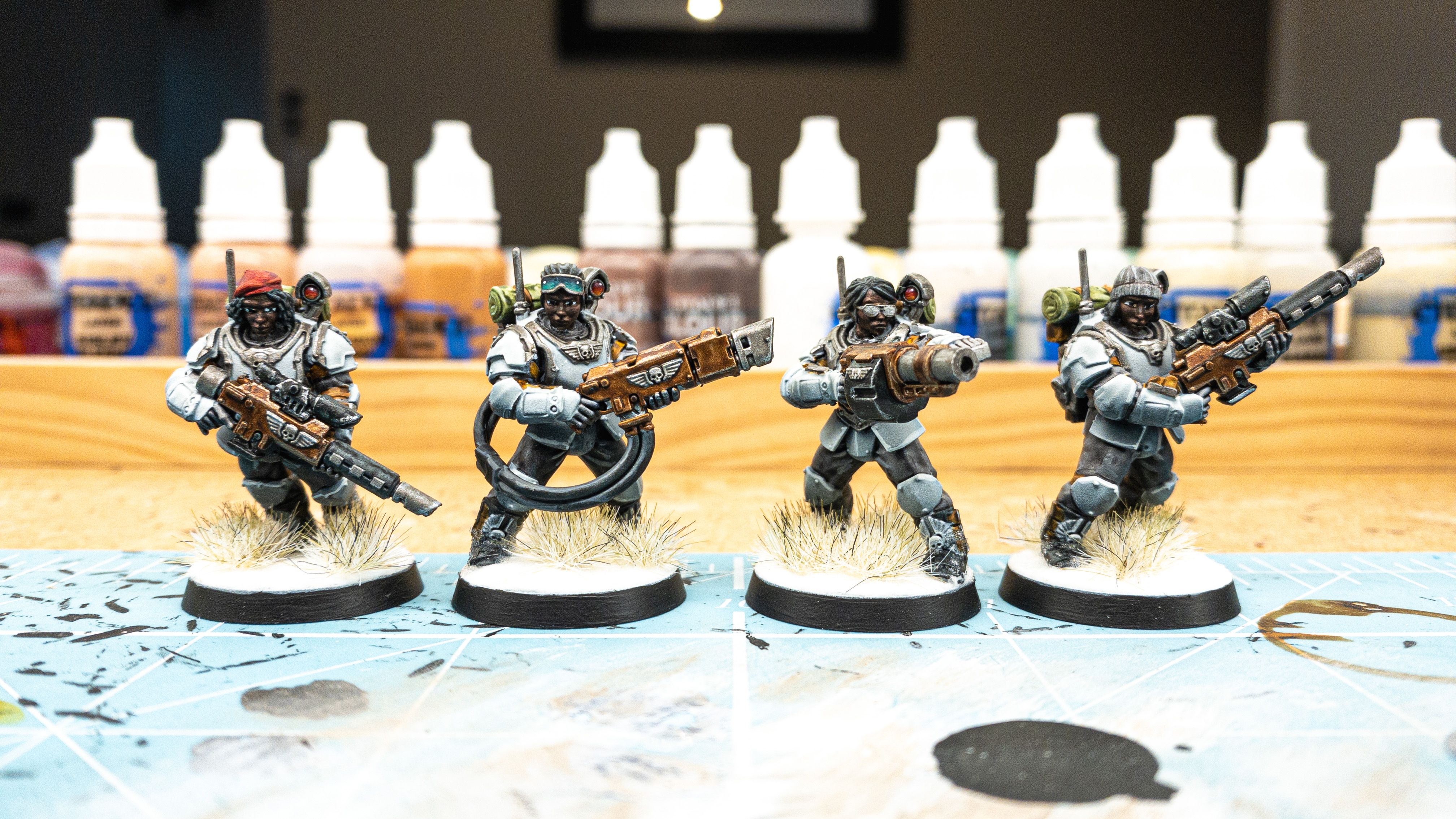 A photo of four Warhammer 40,000 miniatures. They're all regular human troops with big armour and various guns, but the stock male heads have been replaced with third-party female ones from a company called Statuesque Miniatures. The skin colour is very dark but with really nice subtle shading, and the one I called out with the goggles has them pulled up on her forehead. The goggles have a really nice shade going from very dark green down to a lighter green so it looks like they're some sort of futuristic night vision or something.