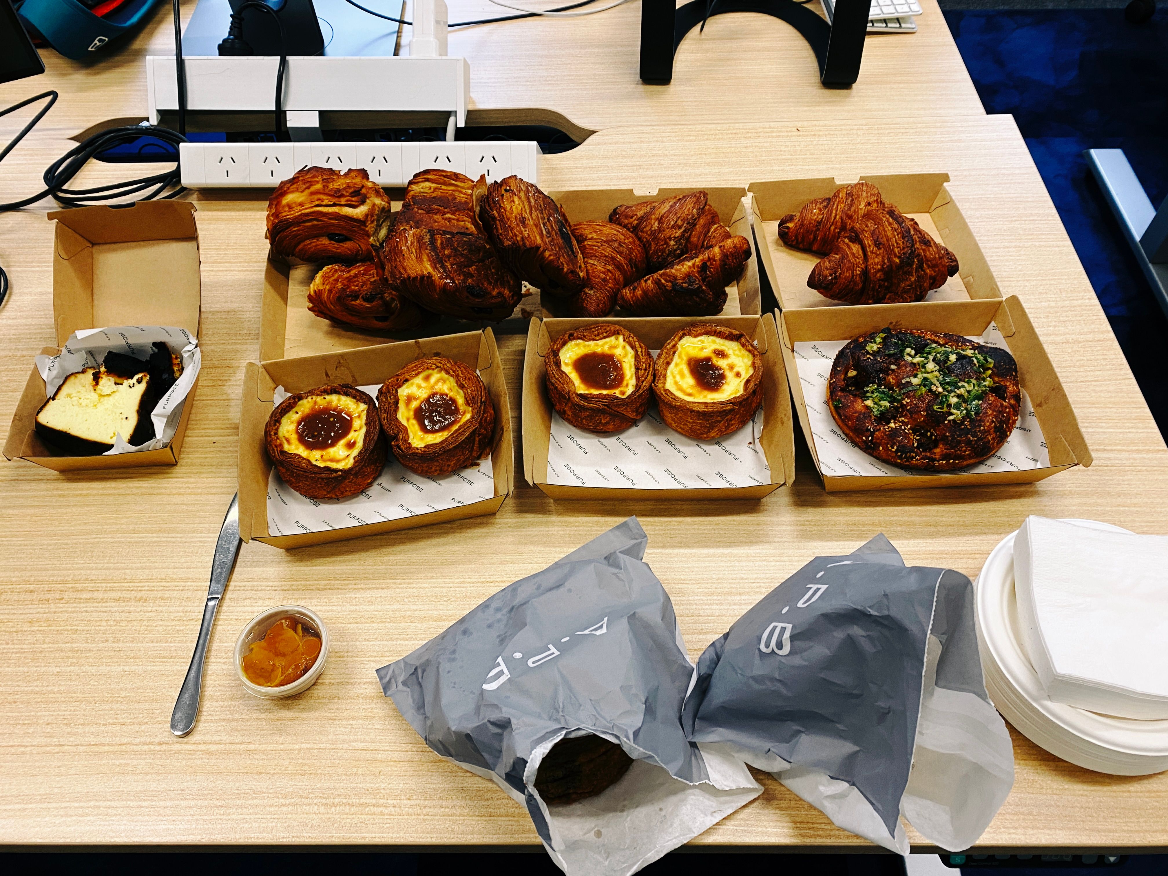 A photo of a bunch of pastries and sweets (croissants, big cookies, etc.) sitting on an office desk.