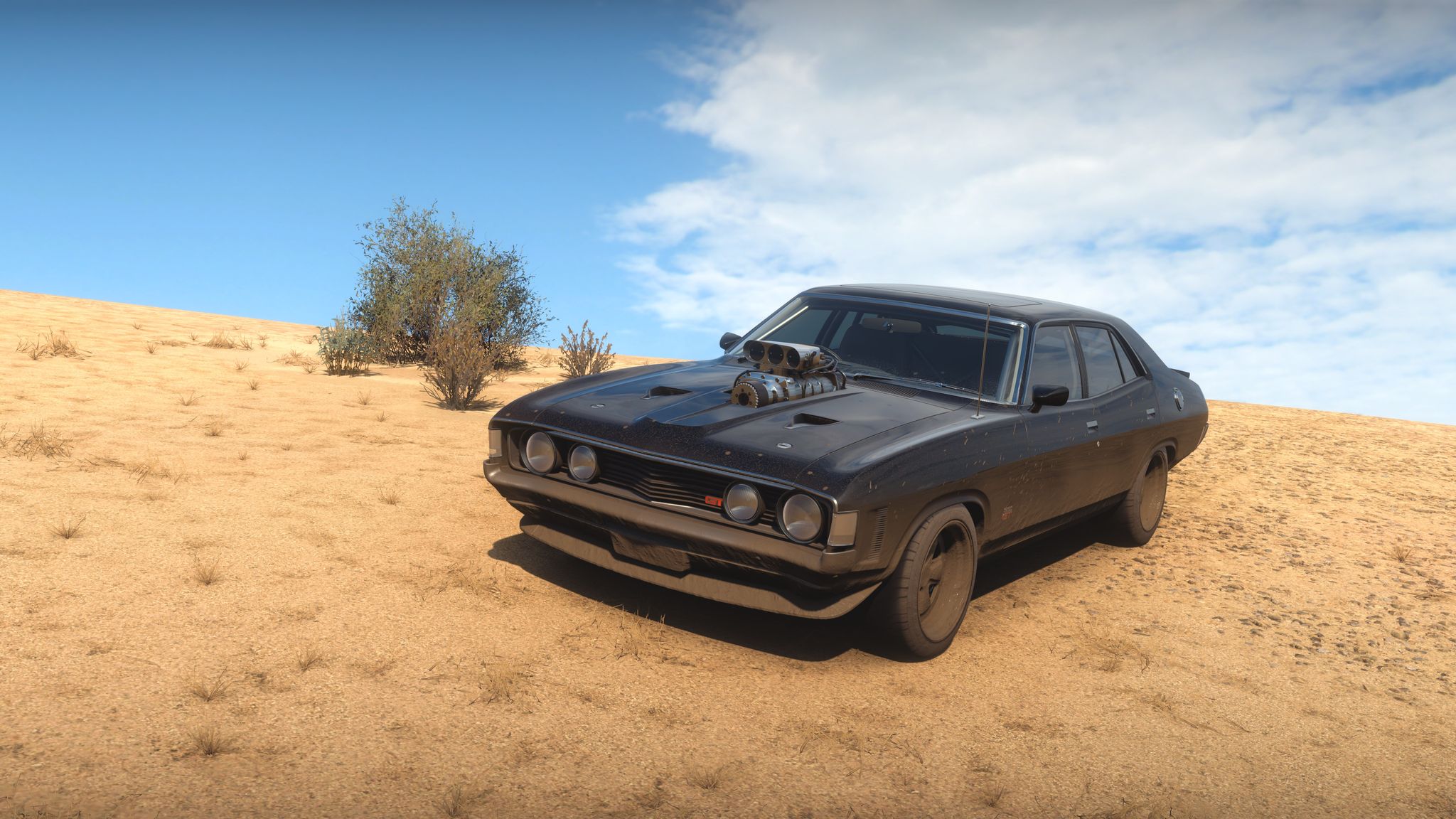 A screenshot from Forza Horizon 5 of a black 1972 Ford Falcon GT-HO muscle car with the engine poking out of the bonnet, looking like something directly from Mad Max. It's got mud spattered on the front and along the sides and is parked on a bleak-looking bit of sandy desert.